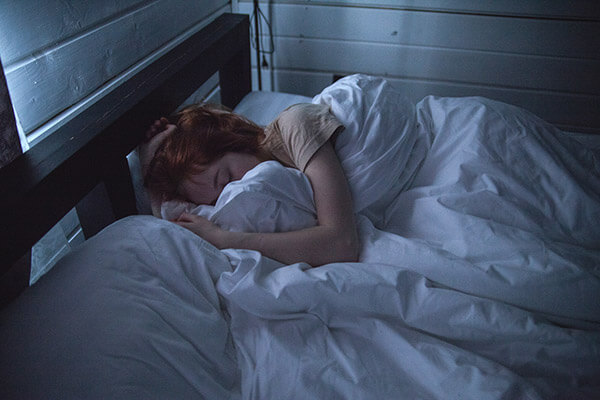 Mujer durmiendo en una cama con sábanas blancas